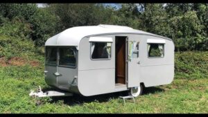 Ein restaurierter grauer Vintage-Wohnwagen auf einer grünen Wiese.
