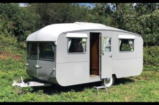 Ein restaurierter grauer Vintage-Wohnwagen auf einer grünen Wiese.