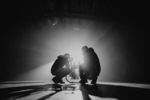 Zwei Filmschaffende richten eine Kamera im Gegenlicht einer starken Lampe aus