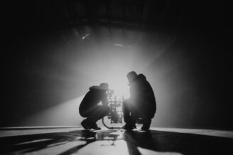 Zwei Filmschaffende richten eine Kamera im Gegenlicht einer starken Lampe aus