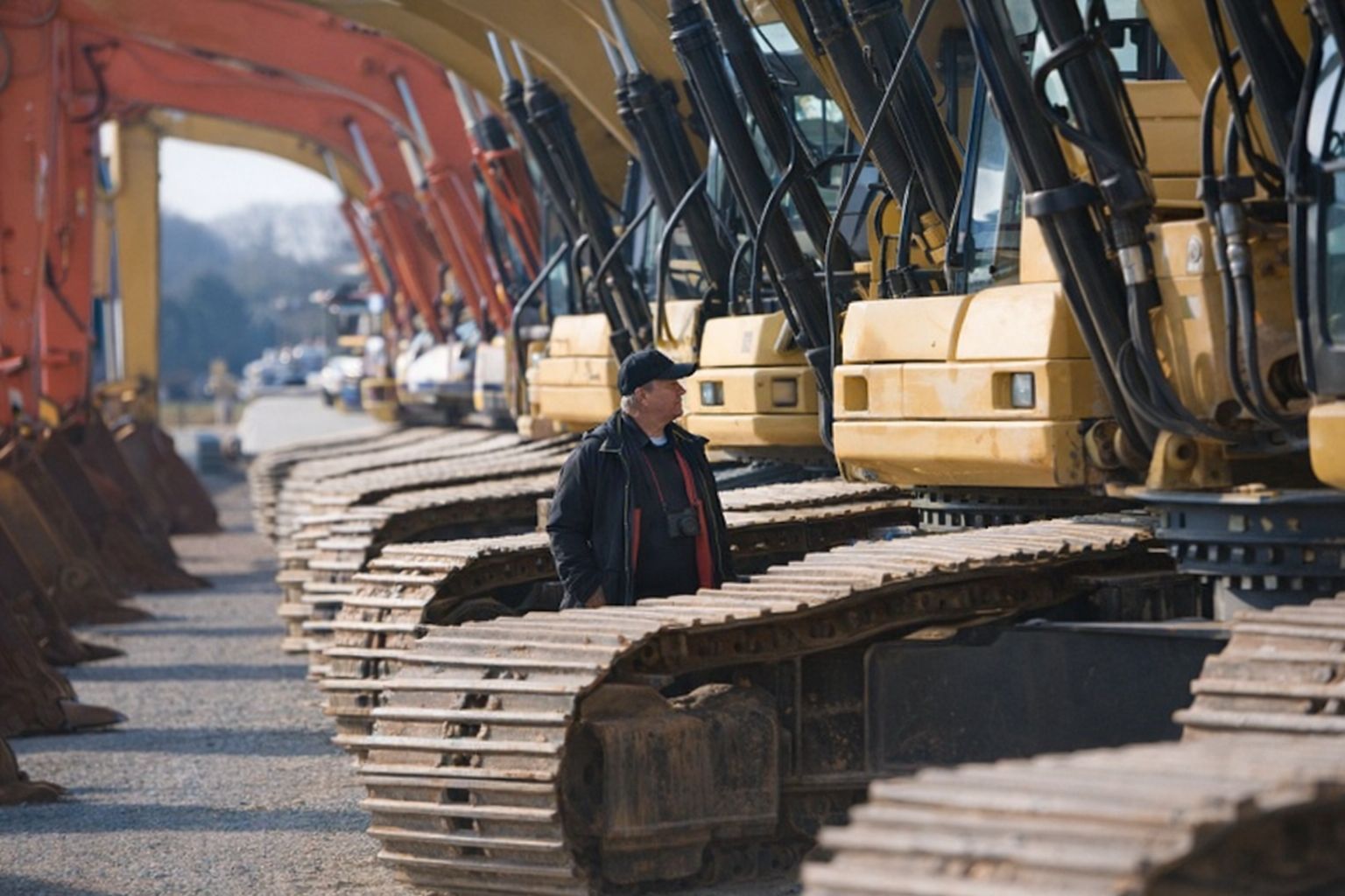 Mann begutachtet eine Reihe gebrauchter Kettenbagger auf einem Auktionsgelände.
